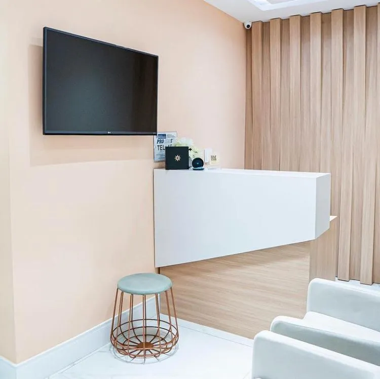 Recepção do consultório, com balcão branco, painel de madeira e poltronas